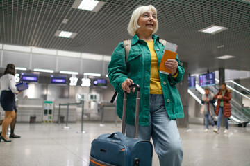 Traveler tourist happy smiling joyful fun mature elderly senior lady woman 55 years old with hand luggage, backpack holds passport and waits for flight travel at international airport terminal. 