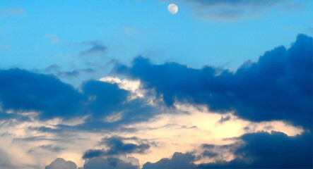 Menacing abstract blue sky with dark and light clouds Cumulus and moon above. Topics: weather, meteorology, cosmos, atmosphere, air space, cloudy, stormy, climate