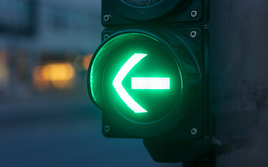 Close-up of a green traffic light with an arrow pointing left, indicating a signal to proceed.