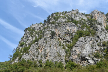 Mountain with rocks, trees and blue sky in the background.
