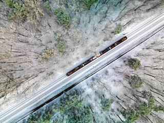 A suburban passenger train travels through a snow-covered forest after the first snowfall, aerial...
