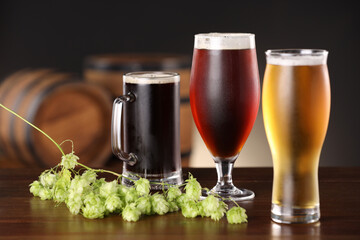 Glasses with different types of beer and fresh hops on wooden table in bar