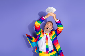 Elderly man in rainbow suit joyfully holding money against a vibrant purple background