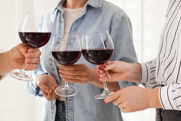 People clinking glasses of red wine indoors, closeup