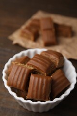 Tasty sweet caramel candies in bowl on wooden table, closeup