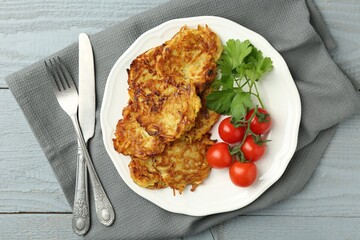 Delicious potato pancakes with tomatoes and parsley served on gray wooden table, flat lay
