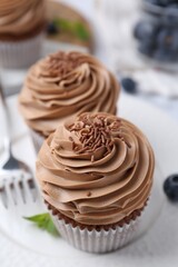 Tasty cupcakes with chocolate cream and blueberries on table, closeup