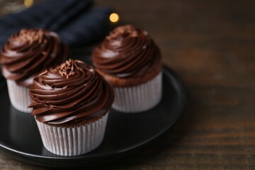 Tasty cupcakes with chocolate cream on wooden table, closeup. Space for text