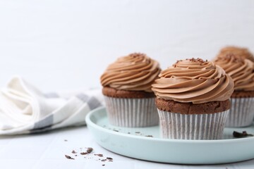 Tasty cupcakes with chocolate cream on white tiled table, closeup. Space for text