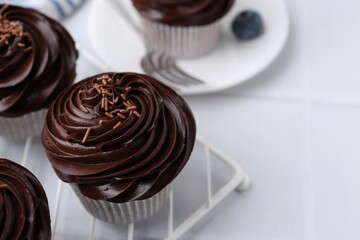 Tasty cupcakes with chocolate cream on white tiled table, closeup. Space for text