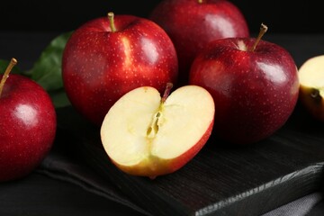 Whole and cut ripe red apples on black table, closeup