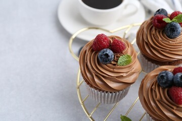 Tasty cupcakes with chocolate cream and berries on white table, closeup. Space for text