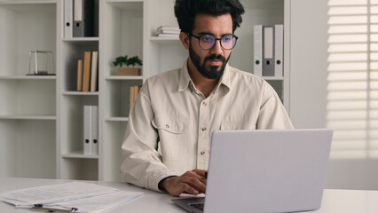 Arabian man Indian muslim ethnic businessman employee manager sit in corporate office with laptop smiling business entrepreneur millennial male working online digital data browsing computer internet