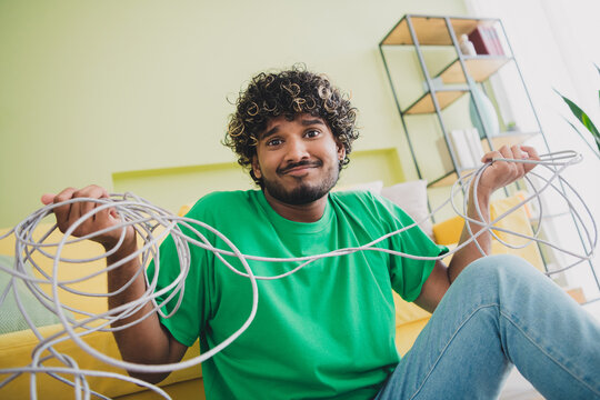 Photo of nice young man shrug shoulders hold messy tied cable wear t-shirt modern green interior apartment indoors