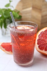 Glass of drink with chia seeds and grapefruit on white tiled table, closeup