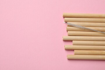Bamboo drinking straws and cleaning brush on pink background, top view. Space for text