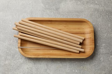Bamboo drinking straws and cleaning brush on grey textured table, top view