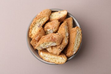 Tasty almond biscuits (Cantuccini) in bowl on beige background, top view