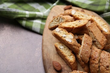 Tasty almond biscuits (Cantuccini) and nuts on brown textured table, closeup. Space for text