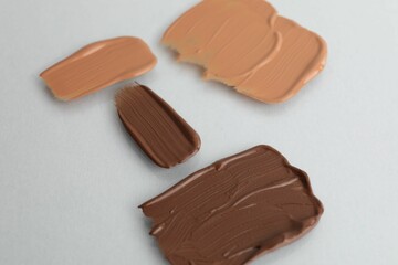 Samples of different foundations on light grey background, closeup