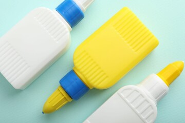 Bottles of glue on light blue background, flat lay