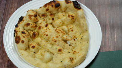 A delicious piece of naan bread set on a white plate, its surface beautifully charred and dotted with golden-brown spots.