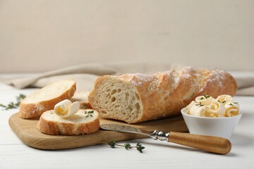 Cut baguette with butter and herbs on white wooden table