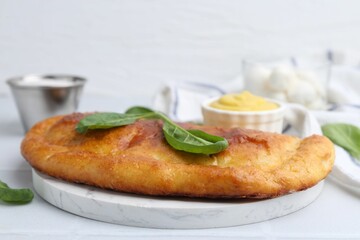 Tasty calzone with basil and sauce on white table, closeup
