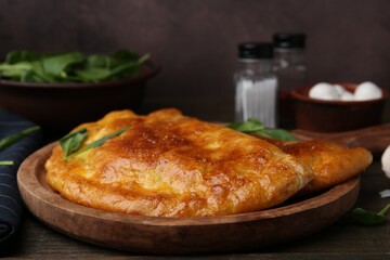 Tasty calzones with basil on wooden table, closeup