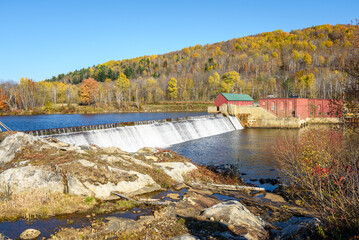 Small dam part of a old hydroelectric power station on  a mountain river on a clear autumn day. Autumn colours and blue sky.