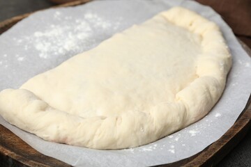 Uncooked calzone pizza on wooden board, closeup