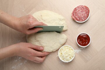 Making calzone pizza. Woman cutting dough into pieces at wooden table, top view
