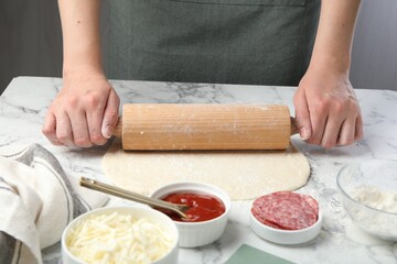 Making calzone pizza. Woman shaping dough with rolling pin at white marble table, closeup