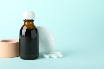 Topical iodine, cotton pad, swabs and adhesive bandage on light blue background. Space for text