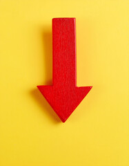 Red wooden arrow pointing down on yellow background. Business, market decline or economic.
