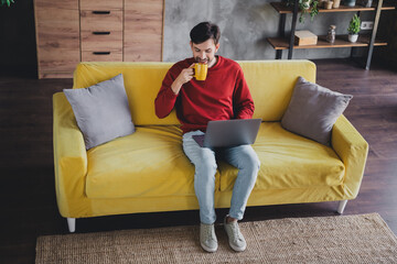 Young man enjoying a relaxed day at home with coffee and laptop on yellow sofa