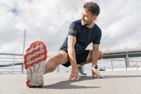 Athlete stretches outdoors on city sidewalk under cloudy sky during daytime workout session