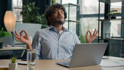 Calm Arabian latin man Indian businessman meditate at office desk zen meditation relaxed male business CEO employer control emotion reduce stress relief harmony balance peace relax computer work pause