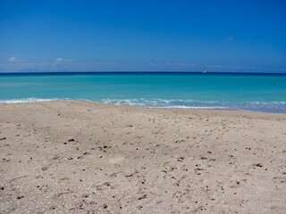 Pristine tropical beach with turquoise waters and a sailboat.