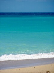 Sandy beach waves and bright turquoise waters meeting the horizon.