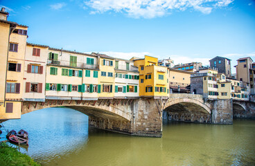 The Ponte Vecchio, the stone, pedestrian bridges in Tuscany, stands on its arched columns with its various retail shops open for business, shining in the sun above the Arno River in Florence, Italy.