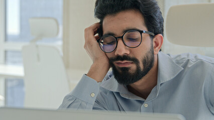 Tired lazy Indian man Arabian businessman manager bored yawn at office desk boring computer work online low energy burnout sleeping exhausted tired male business entrepreneur laptop working boredom