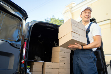 Delivery worker unloading boxes from van in bright daylight outside a commercial building