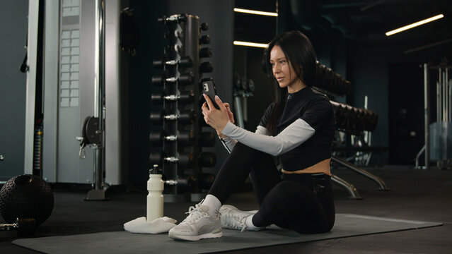 Female fitness instructor trainer sports blogger influencer Caucasian woman sportswoman talk mobile phone talking streaming workout record video tutorial in gym teaching online exercise in sport club
