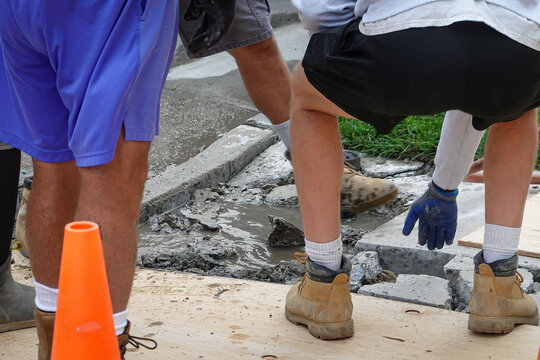 Lower body of Several workers wearing work boots around water filled hole in concrete by a street