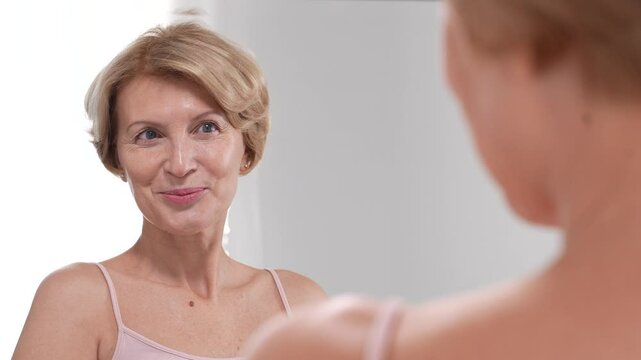 Youthful gorgeous middle-aged woman is happy while looking at her appearance. Confident modern female in love with her authenticity. Slo mo