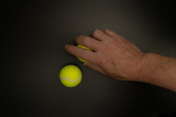 Hand grabbing tennis ball on black background with copy space