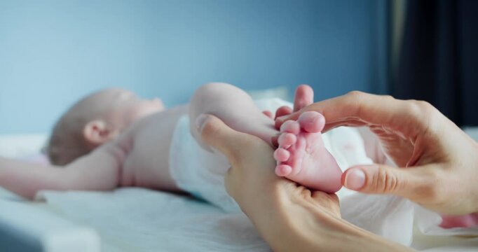 Mother massaging newborn infant baby feet with thumbs tender touch parenting. Mother playing with baby feet. Stretching and exercises for baby development concept