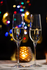 concept of celebrating christmas and new year, two glasses of champagne on the background of candles and colorful garlands, warm home traditional festive atmosphere