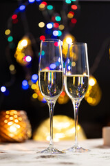 concept of celebrating christmas and new year, two glasses of champagne on the background of candles and colorful garlands, warm home traditional festive atmosphere